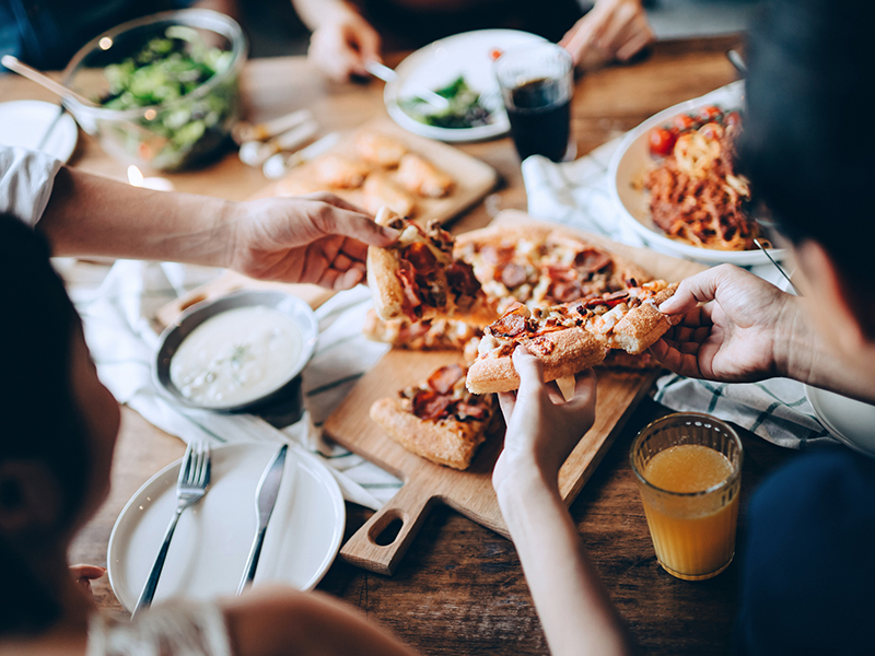 Close up of a young group of friends passing and serving food while enjoying together.