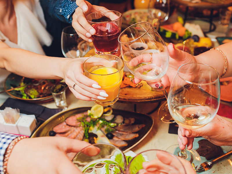 Close up shot of group of people clinking glasses with wine or champagne in front of bokeh background